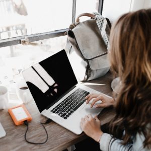 girl wearing grey long-sleeved shirt using MacBook Pro on brown wooden table taking an online course in UK